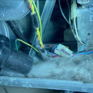 Technician cleaning the inside of a dryer using tools to remove lint and debris.